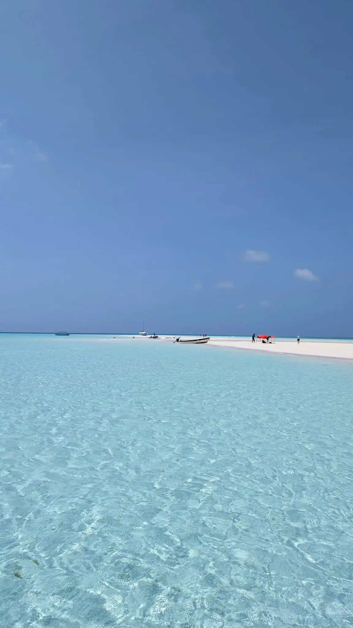 Two boats pulled up on a distant sandbank across bright turquoise shallows.