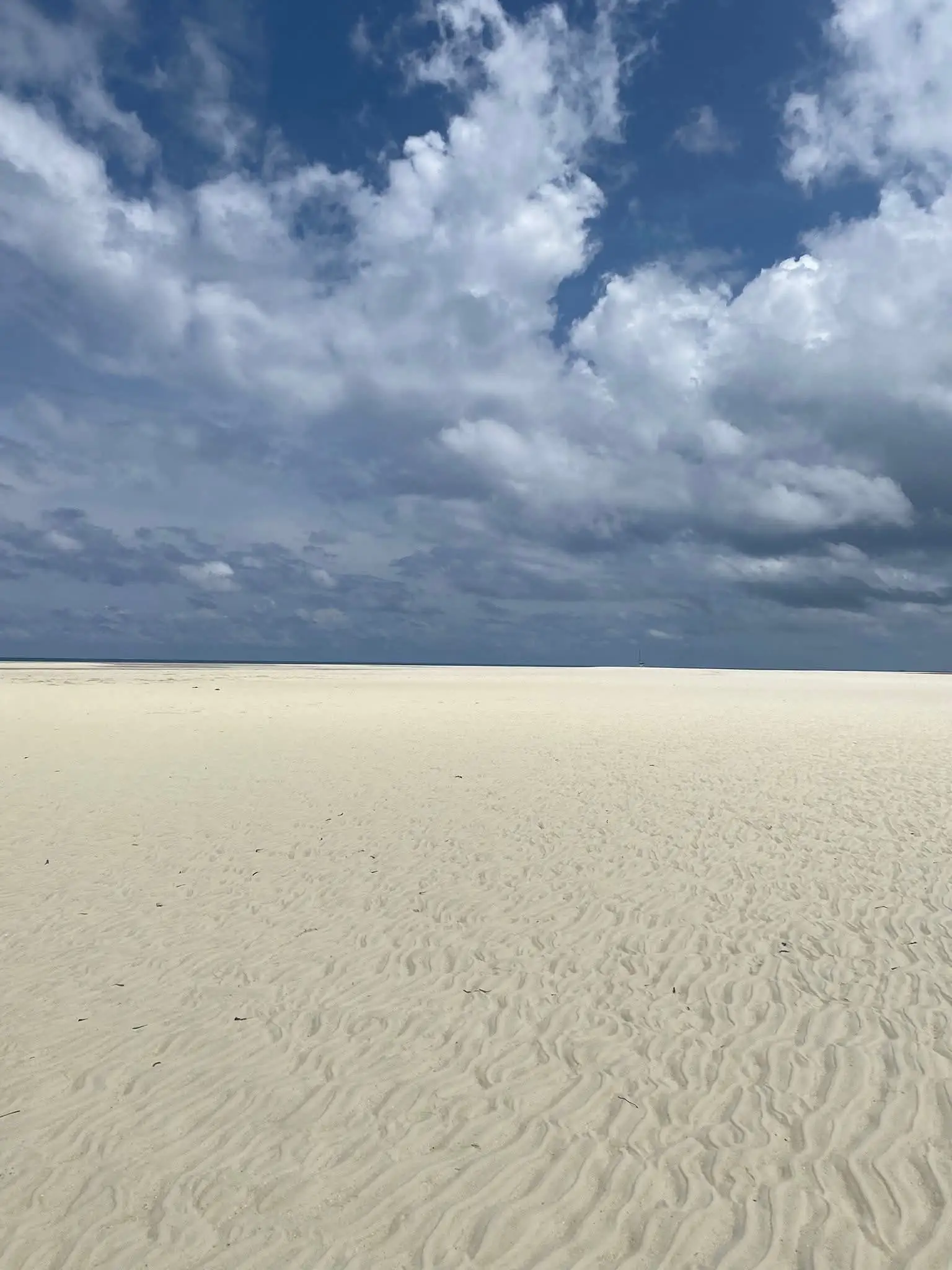 Wind-rippled white sand stretching to the waterline under tall clouds.