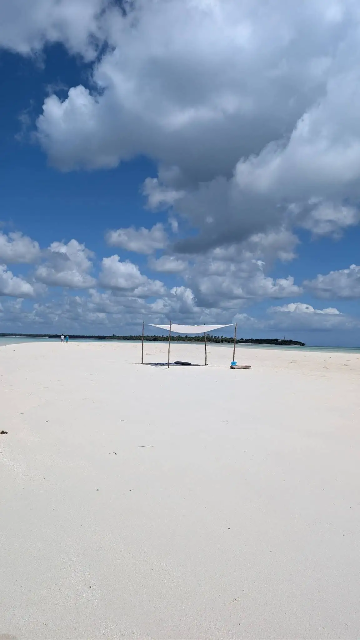 A white canvas sun shade on poles, the only structure on a bare sandbank.