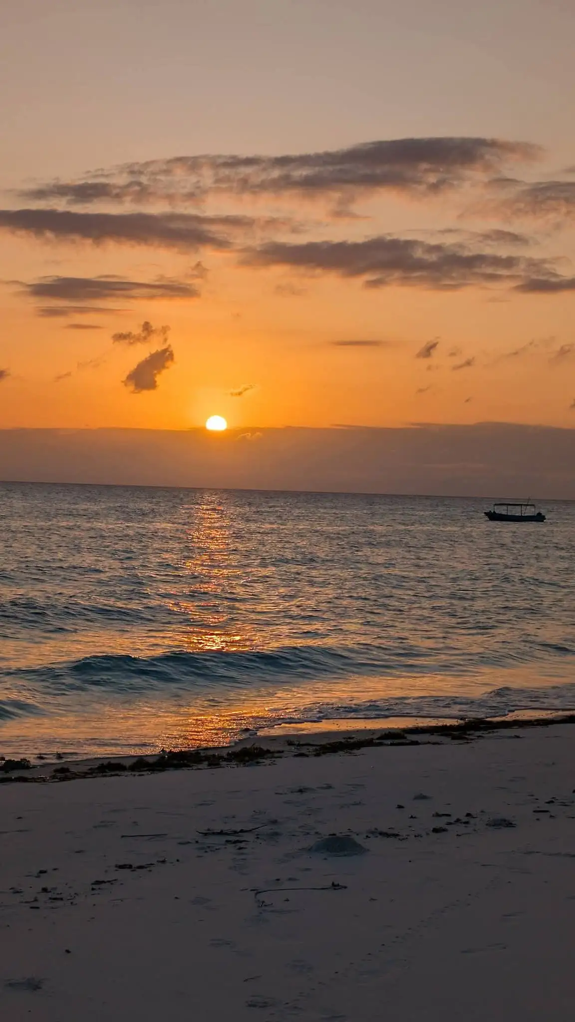The sun setting into the sea, laying an orange path across the water towards the beach.