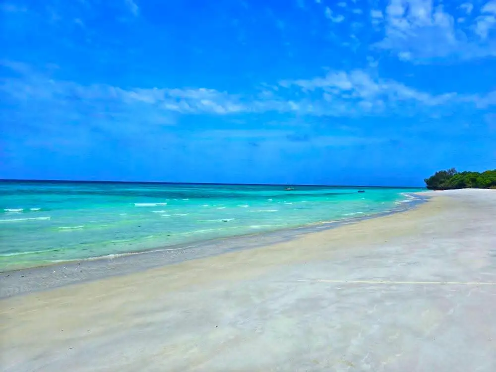 Turquoise water breaking along a wide, empty white beach under a deep blue sky.